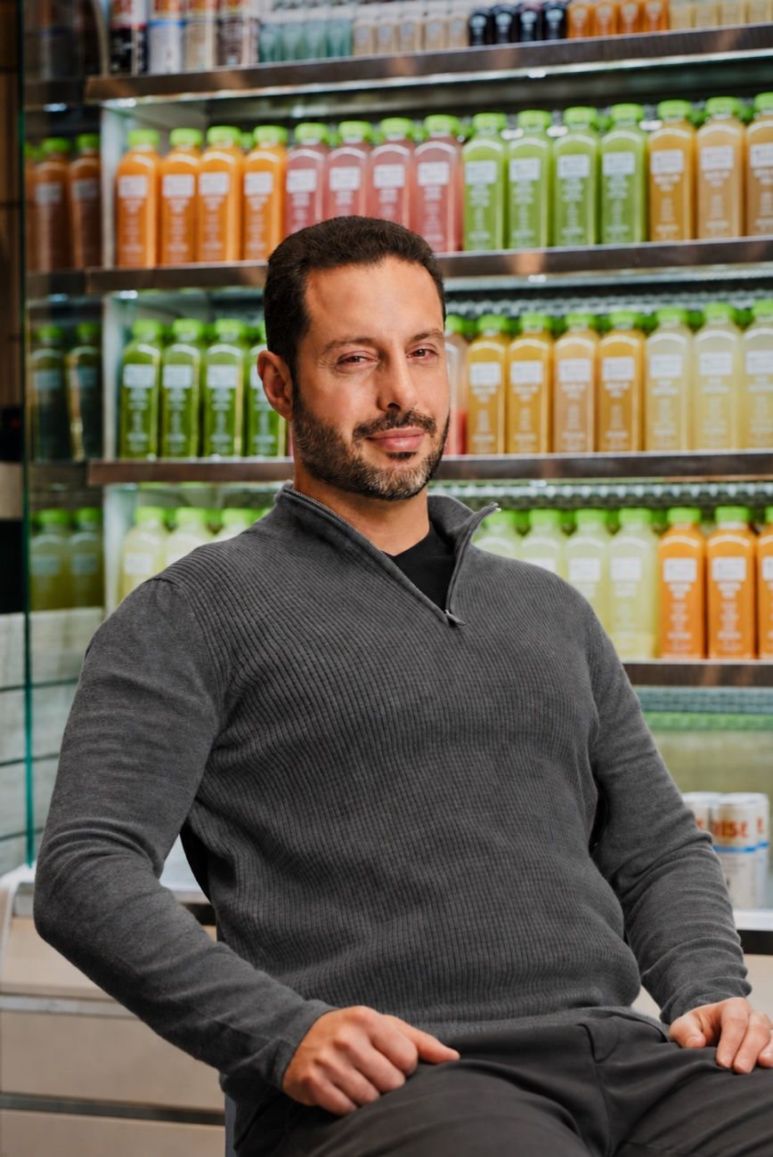 Ross Franklin seated in a Pure Green shop beside the cold-pressed juice display